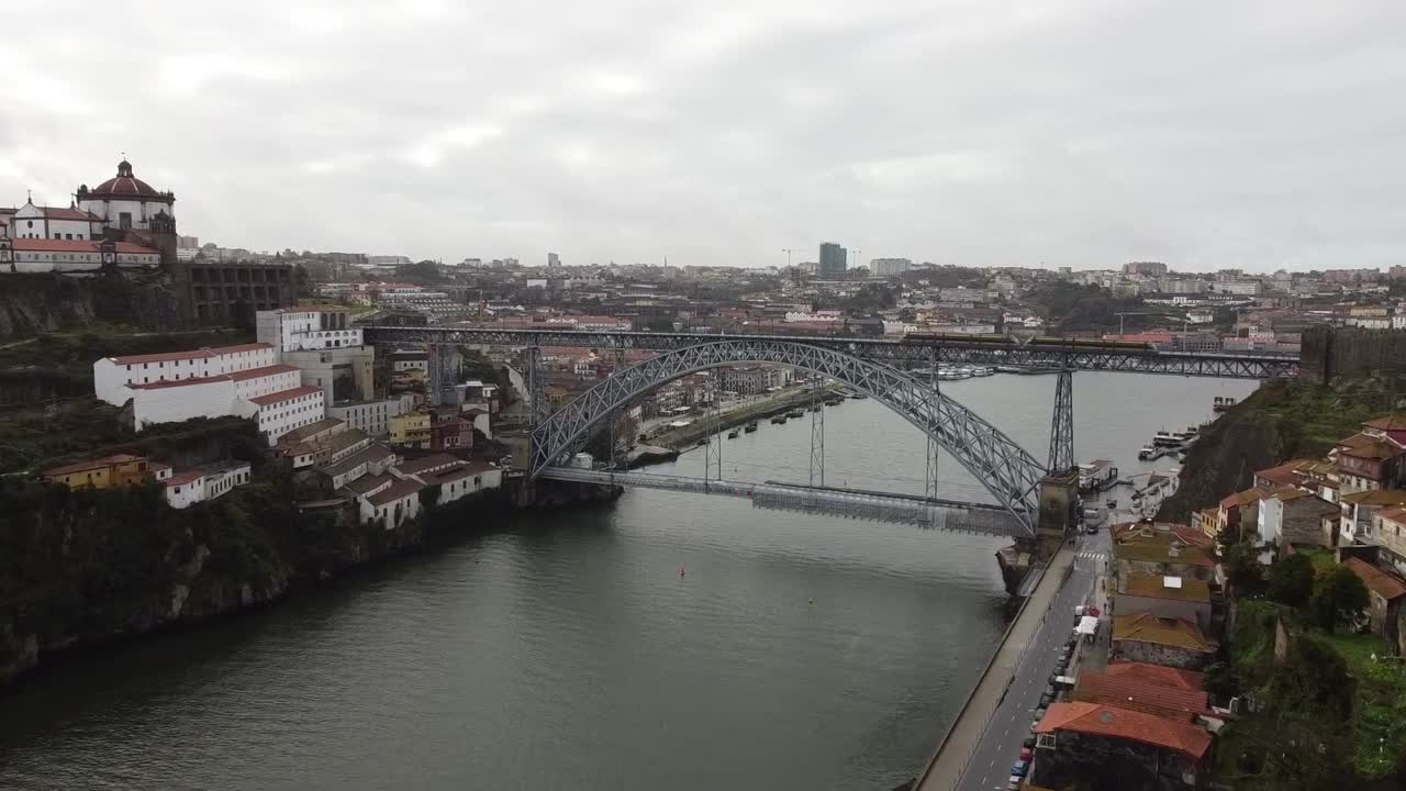 Aerial drone view of Dom Luis I Bridge crossing Douro River in Porto, Portugal, with historic buildings, moody clouds, and cityscape showing iconic architecture and riverside charm