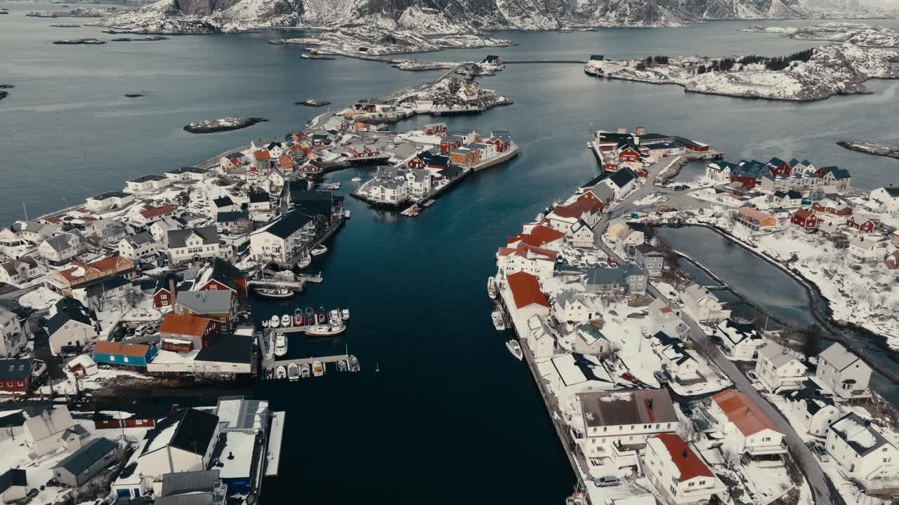 Snowy Rocky Mountain From Henningsvaer Fishing Village By The Sea In Nordland, Norway. - aerial pullback shot