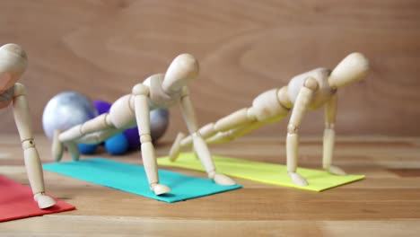 wooden figurines exercising push-ups on colored exercise mat in front of gym balls against wooden ba