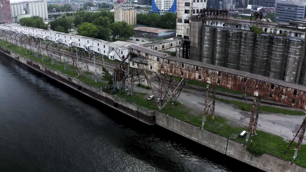 Aerial view of rusted industrial silos with a modern city skyline backdrop. A stunning contrast of urban decay and sleek architecture. Montreal's Old Port docks.