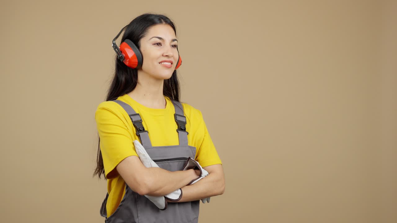 Woman in work overalls and ear protection looking to the side
