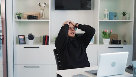 The-young-man-is-sitting-behind-a-laptop,-rooting-for-someone,-getting-nervous-and-saddened-by-the-loss