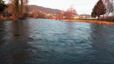 Aerial-drone-pullback-shot-flying-up-above-the-river-Limmat-and-revealing-the-town-of-Unterengstringen-in-the-background-in-the-canton-of-Zürich,-Switzerland