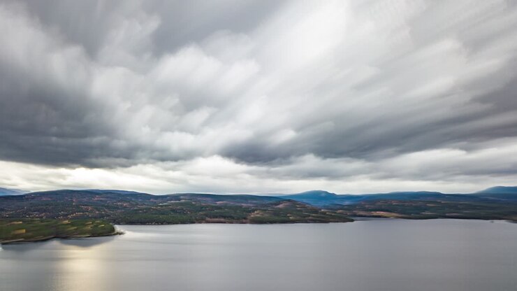 Thick white clouds rushing above the calm dark water of the fjord