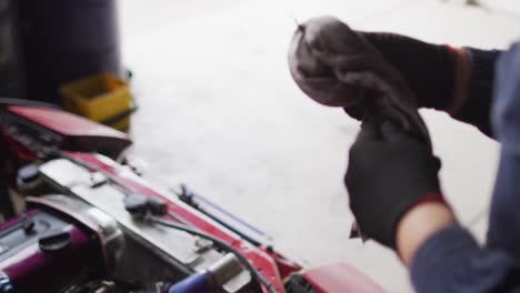 Mid-section-of-female-mechanic-cleaning-equipment-of-the-car-with-a-cloth-at-a-car-service-station