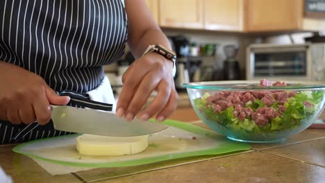 Cutting-a-round-of-mild,-white-cheese-to-add-to-a-chopped-salad---ANTIPASTO-SALAD-SERIES