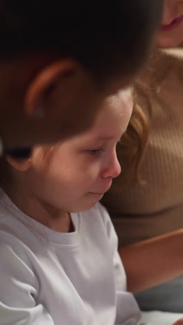 young mother shows vintage faded photos to little daughter and african-american friend recalling family members in living room closeup slow motion