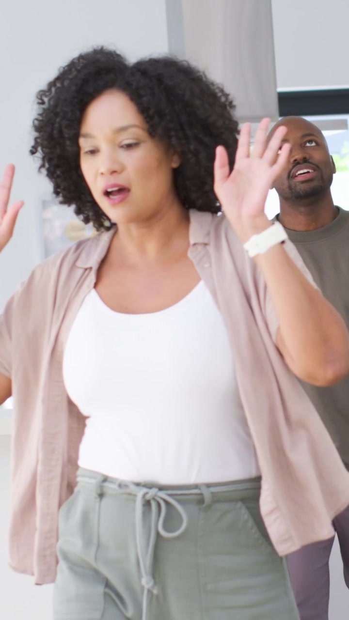 Vertical video: Looking woman turning, waving palm up, calming man at kitchen island, smartwatch