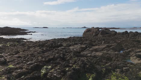 Vuelo-Bajo-De-Drones-Sobre-Rocas-Hacia-El-Mar-Desde-Belle-Greve-Bay-Guernsey-En-Un-Día-Brillante-Y-Tranquilo