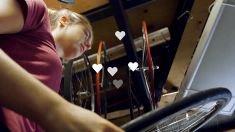 woman repairing bicycle wheel in bike repair business, displaying floating social media heart icons