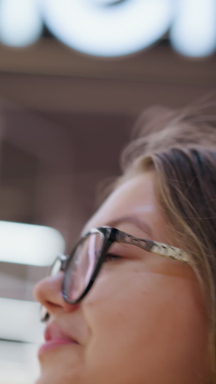 Primo piano di una lavoratrice remota che si sistema i capelli mentre guarda qualcosa sullo sfondo, con una vista sfocata di un negozio, che mostra una rilassante esperienza di shopping o una giornata di lavoro informale