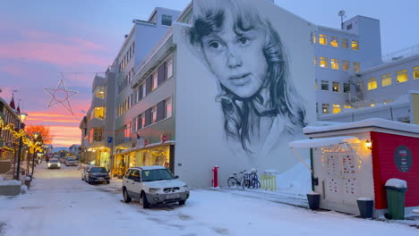 beautiful mural of a girl on an apartment complex in a cozy street lit with christmas lights in akureyri in iceland in winter time