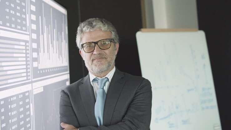Friendly mature finance expert posing near big screen