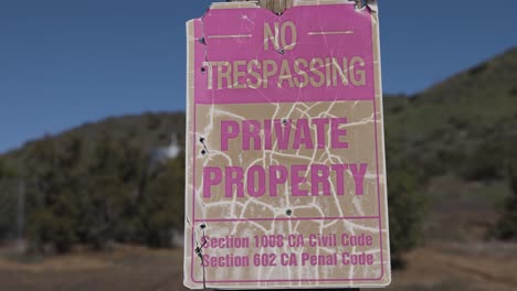 Worn-out-old-no-trespassing-and-private-property-sign,-with-mountains-in-the-background