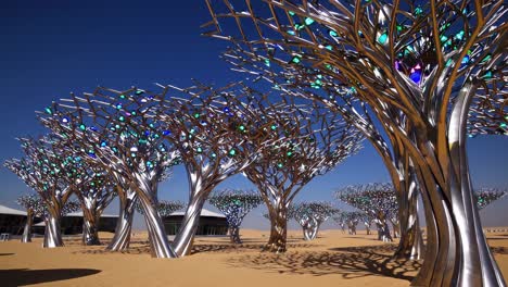 metallic sculptural trees featuring vibrant glass foliage rising from sandy desert terrain, reflecting innovative design against cloudless dubai skyline