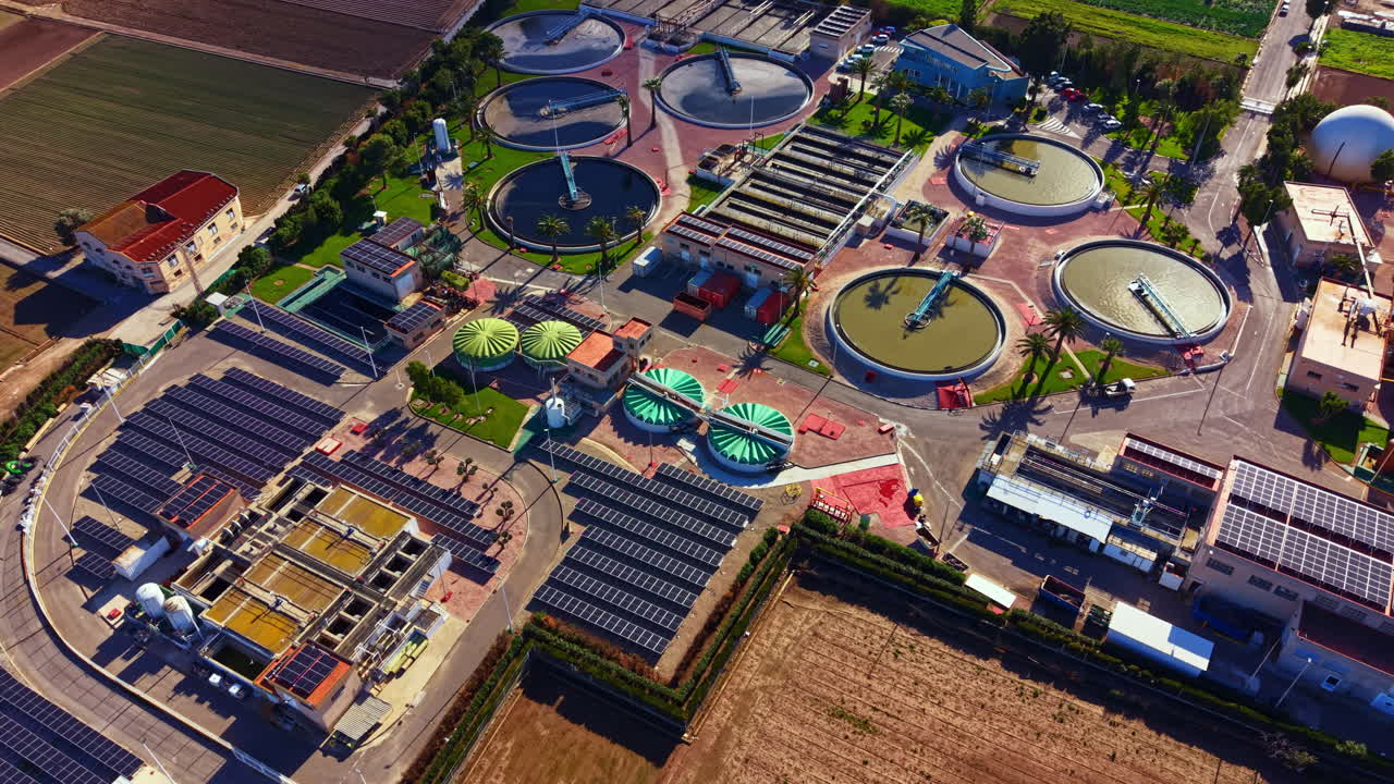 Wastewater treatment facility in a rural area with circular tanks and solar panels in the background under bright sunlight