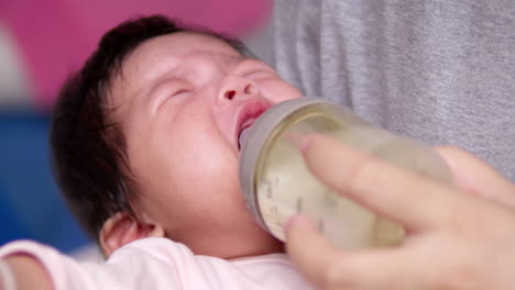 hungry newborn child crying out for its mother to feed her some milk in a bottle, as her mom cradles her in her mom's arms