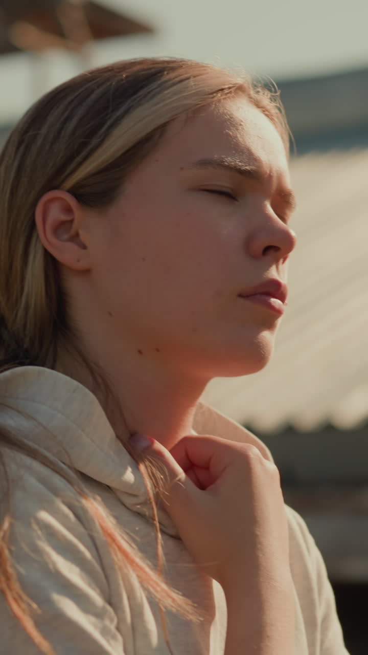 primer plano de una joven pensativa caminando al aire libre en el estadio, la mano tocando suavemente su sudadera con capucha, con un fondo borroso y luz solar suave