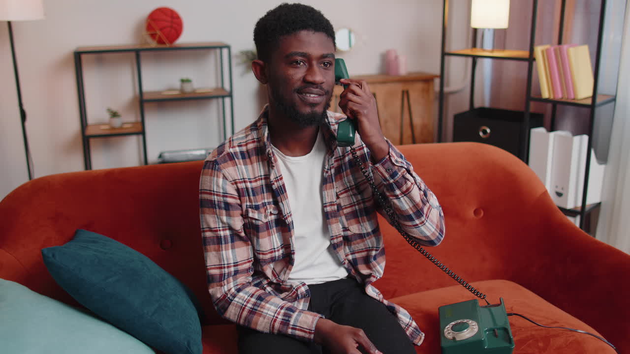 Young adult african american man enjoying talking on retro phone conversation with friends at home