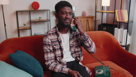 Young-adult-african-american-man-enjoying-talking-on-retro-phone-conversation-with-friends-at-home