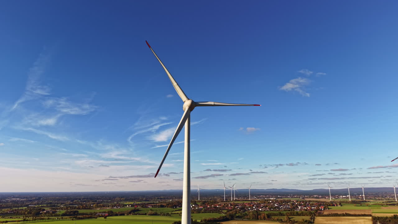 La turbina eolica si erge imponente contro un cielo azzurro brillante, mostrando la bellezza dell'energia rinnovabile e l'armonia della natura in campagna.