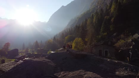 People-gathered-on-top-of-a-rocky-shape-and-old-buildings-around-and-a-landscape-with-trees,-on-the-horizon-the-sun-shining-at-sunset