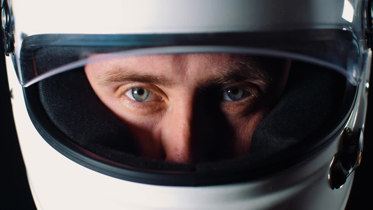 Pria bermata biru tajam melihat ke kamera dan menutup visor helm dalam gerak lambat 4K, close-up wajah.