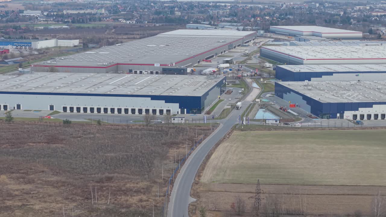 Bred dronepanorering fra luften af en stor, moderne logistikpark med flere lagerbygninger, blå facader, læsseramper, adgangsveje og lastbiler synlige over hele komplekset i Polen