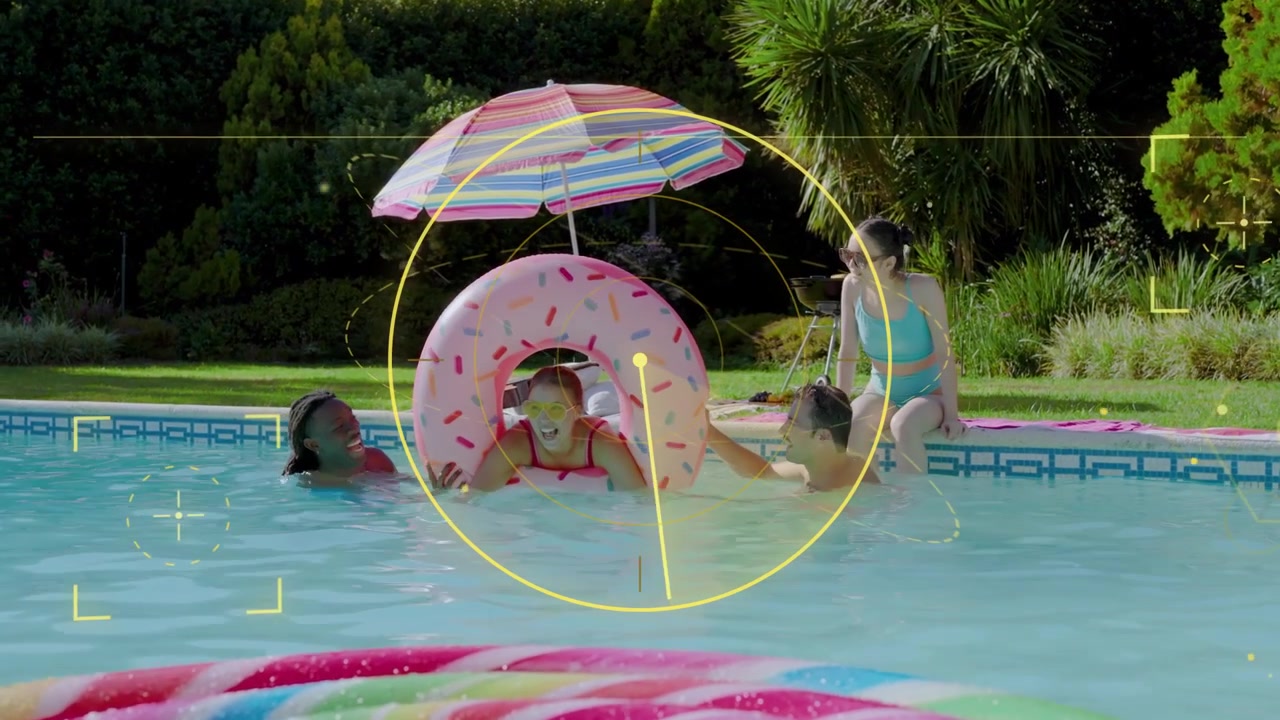 Child pushing through pink donut float to emerge, adults supporting, yellow HUD marking tech
