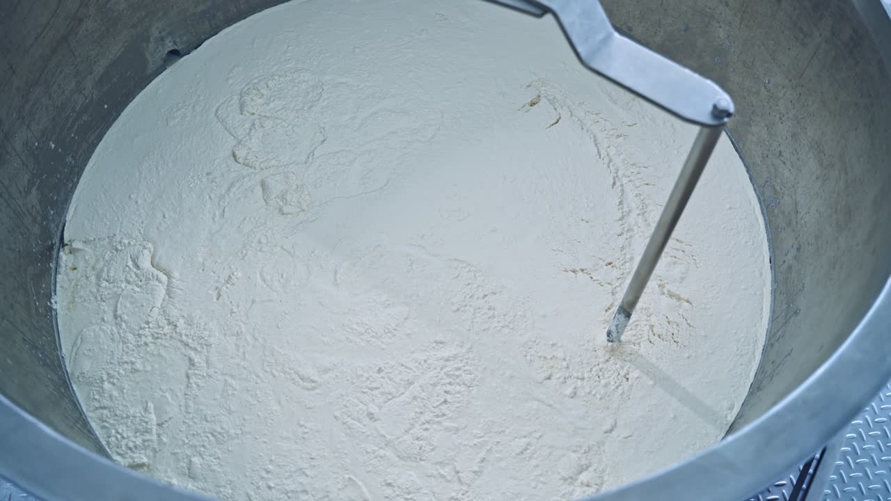 Slow motion of mixer in metal bowl for making cheese. Factory equipment. Metal mixing apparatus boils and mix milk for making cheese at milk products making factory.