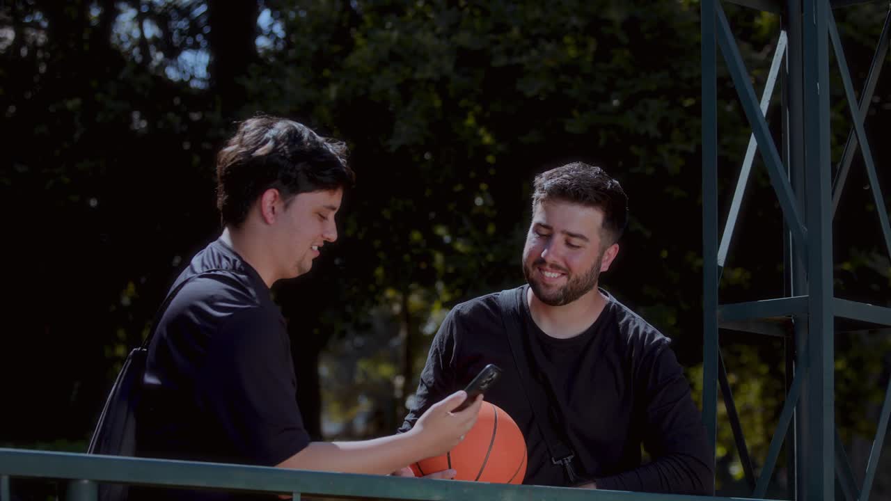 Two friends having fun with a basketball and phone outdoors