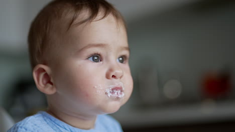 little kid with adorable plump cheeks eats porridge. female hand gives a spoon to a baby and cleans child's mouth. close up.
