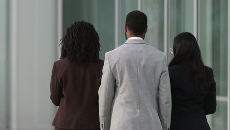 back view of three people wearing suits walking near building