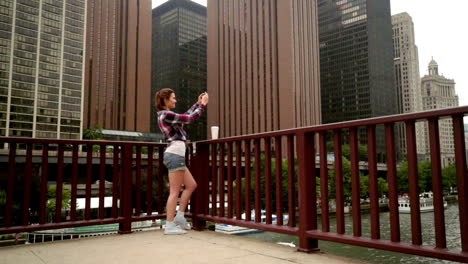 Joven-Hermosa-Mujer-Haciendo-Fotografías-Móviles-De-Los-Rascacielos-De-La-Ciudad-Moderna