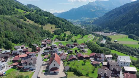 aerial rising wide shot of housing area in swiss suburb at sunny day. summer season in switzerland. green trees along alps mountains. flyover shot