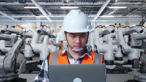 Engineer working on laptop in a factory with robotic arms