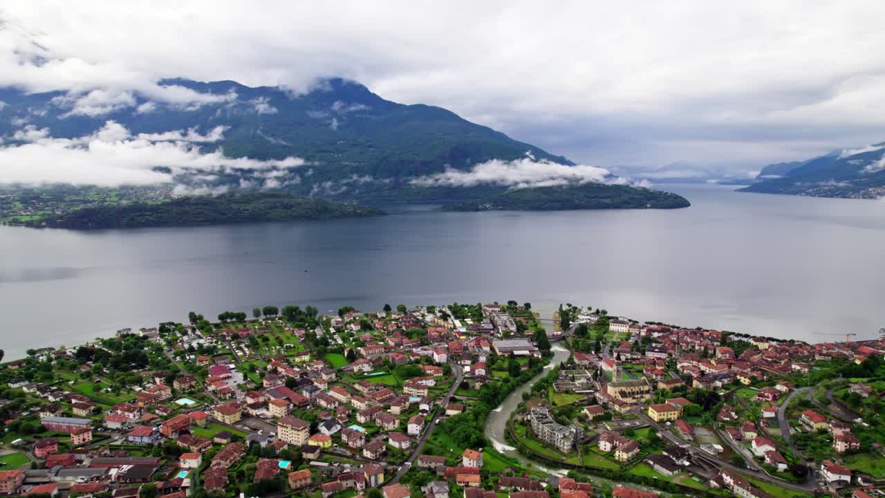 Filmato aereo cinematografico realizzato con drone che vola all'indietro sopra una città storica con tetti rossi, rivelando il Lago di Como e una grande montagna alpina sullo sfondo