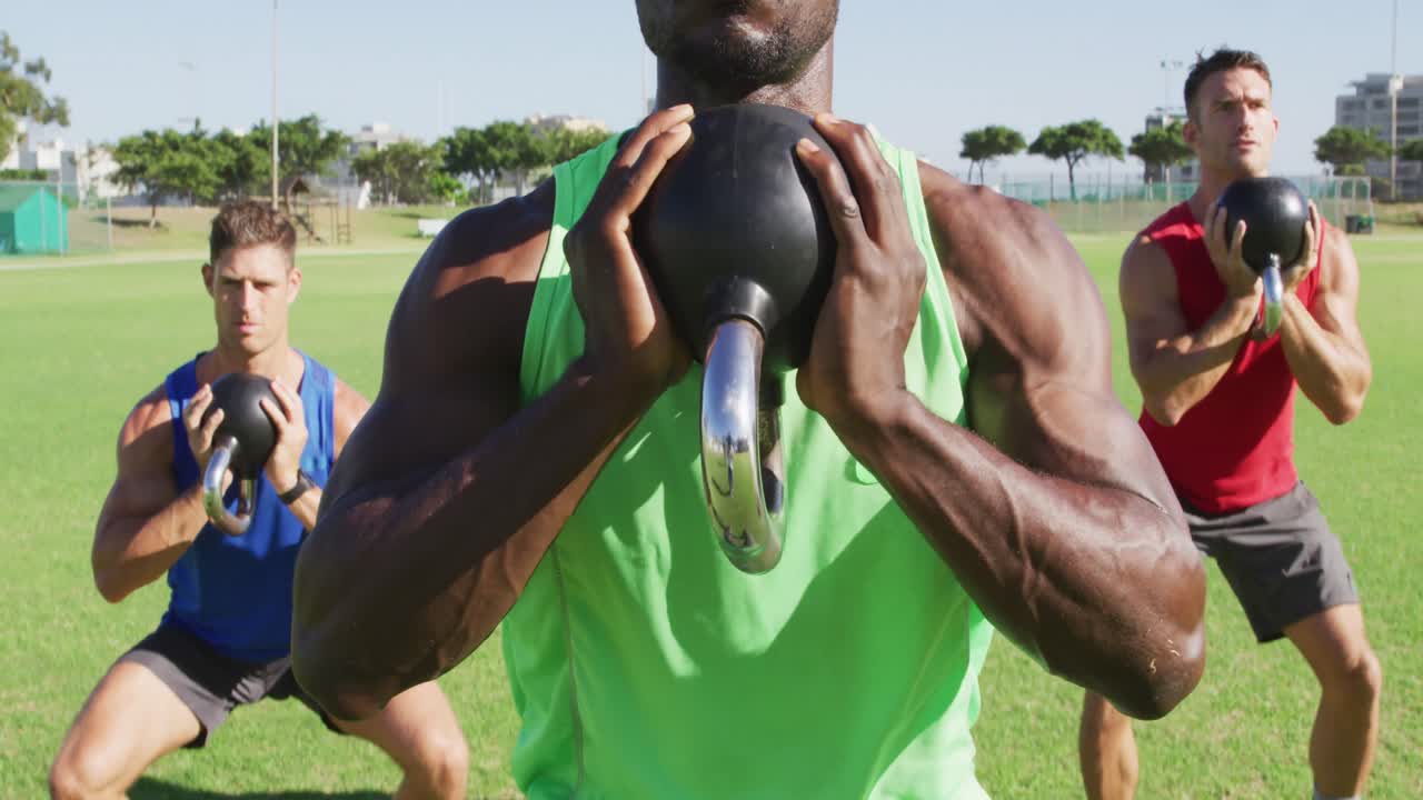 3명의 건강한 남성들로 구성된 다양한 그룹이 야외에서 운동을 하고, 앉아서 케틀벨 무게를 들어 올리고 있습니다.