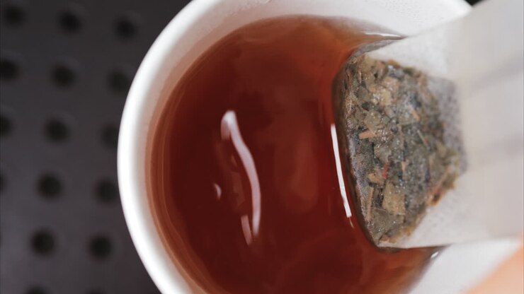 Primo piano di una bustina di tè immersa in acqua calda, che rilascia colore e aroma intensi