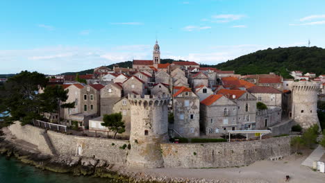 korcula old town houses, tower, and beach by the adriatic sea in croatia. - aerial pullback shot