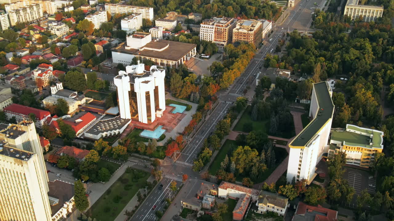 Aerial drone view of Chisinau downtown. Panorama view of multiple buildings, Parliament, Presidency, roads with moving cars and lush trees. Sunset. Moldova
