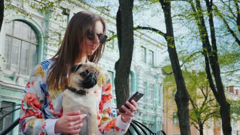 a woman with a dog is sitting on a bench in the park. uses a mobile phone