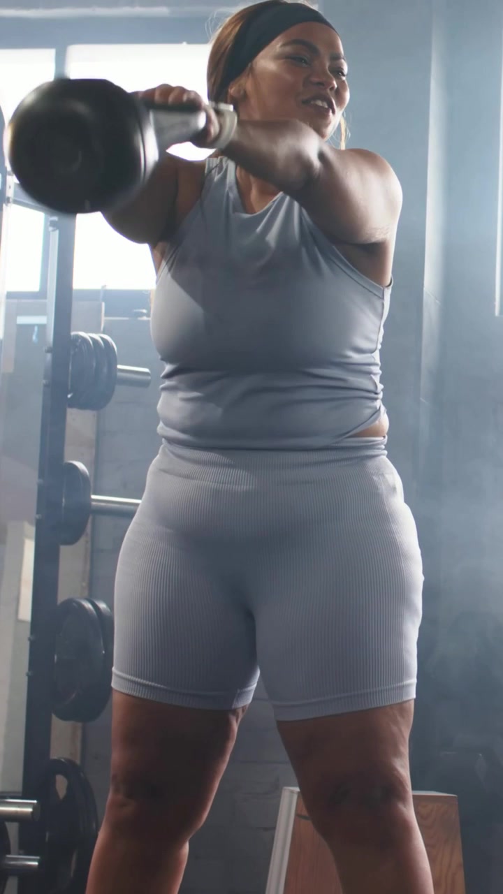 Video verticale: Donna con canotta azzurra che solleva un kettlebell ed esegue degli swing in palestra per la forza.