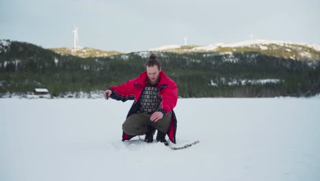 Hombre-Pescando-En-Un-Agujero-De-Hielo-De-Un-Lago-Congelado-Durante-El-Invierno-En-Noruega