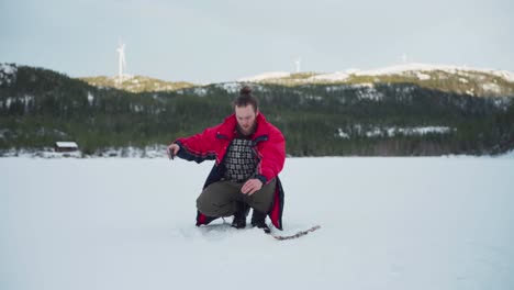 Man-Fishing-On-Ice-Hole-Of-Frozen-Lake-During-Winter-In-Norway