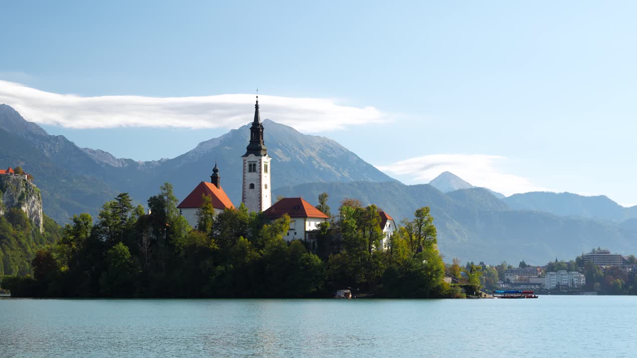 Castello e torre dell'isola del lago di Bled, visti dalla riva con montagne e acqua blu calma in una dolce giornata di sole, panoramica verso sinistra