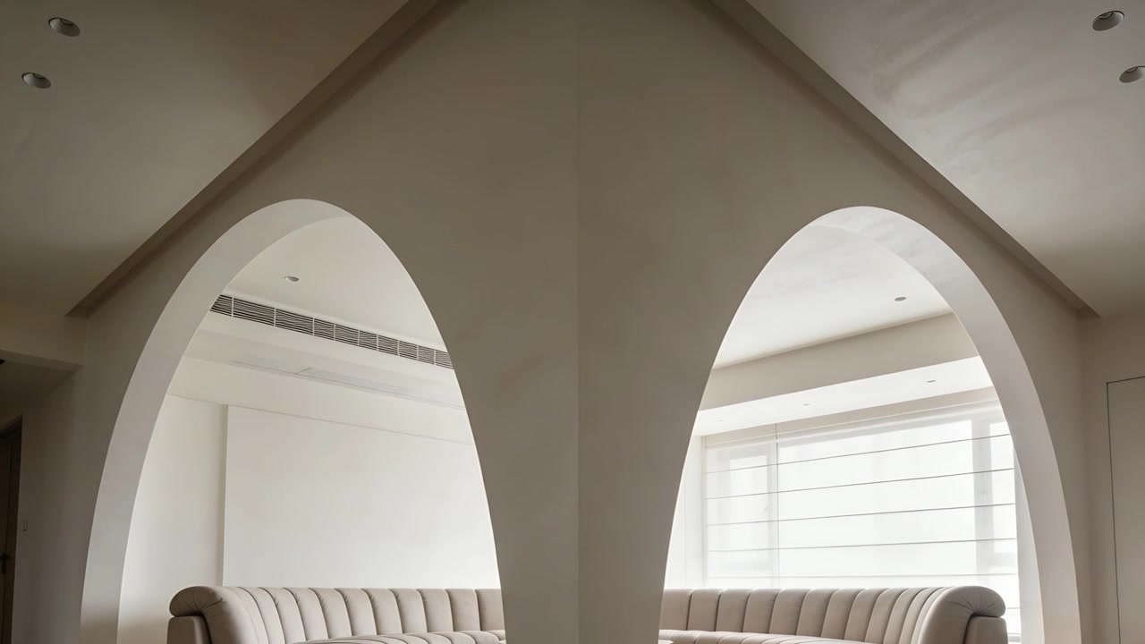 Telecamera inclinata che enfatizza l'apice del soffitto e le luci nel soggiorno, mostrando un divano capitonné e due archi.