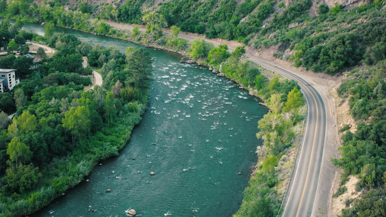 Low, cinematic flyover hugging the river’s path, capturing reflections from the water and shadows from the pines.