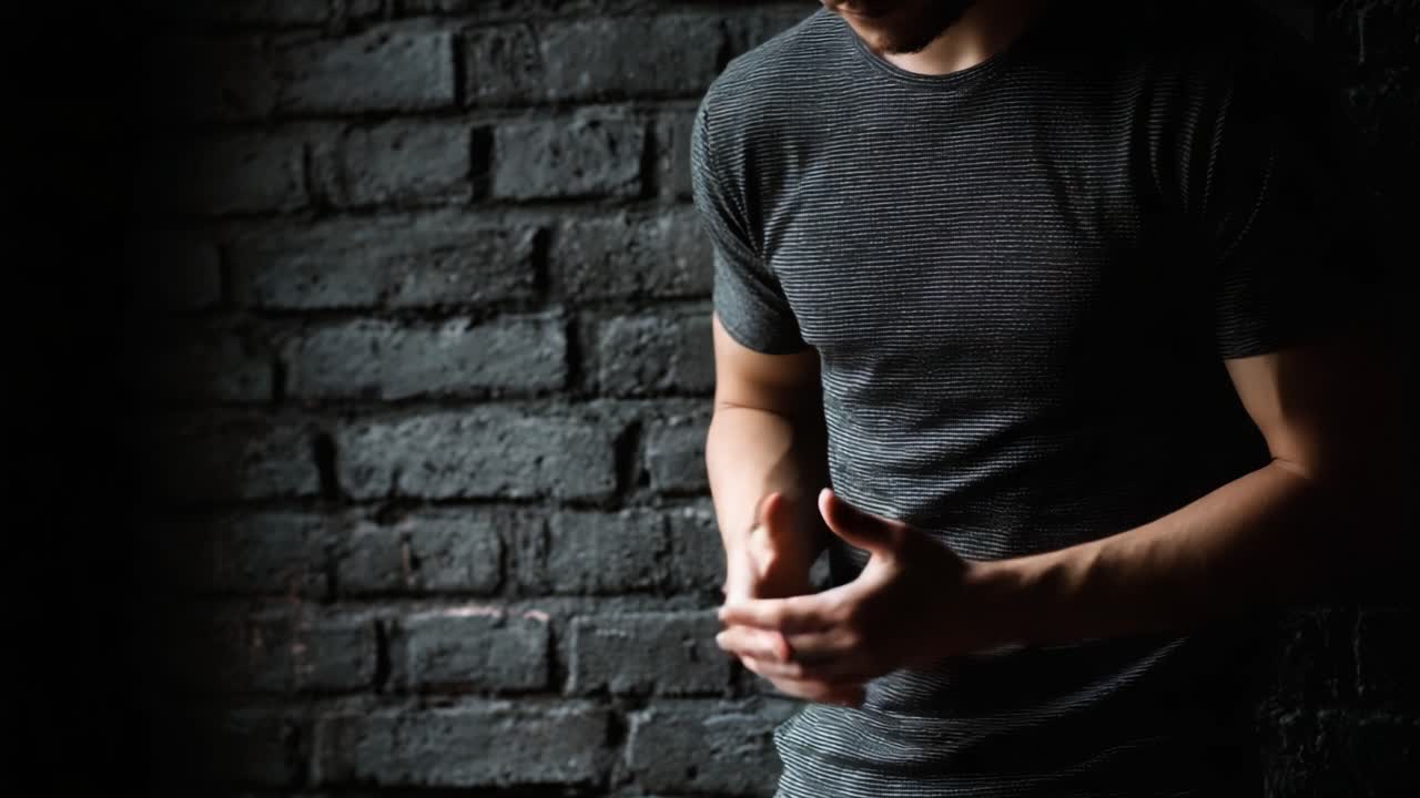 A contemplative moment of a young man standing against a textured wall, conveying a sense of introspection and emotional turmoil in a dimly lit environment