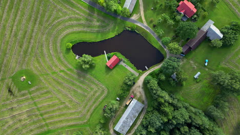 Drone top down descends on rural home compound surrounding peaceful calm lake with freshly mowed grass pattern around dirt road